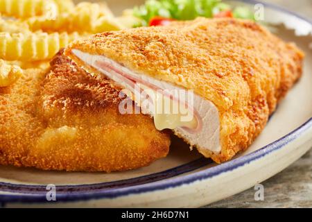 Primo piano di delizioso condon bleu a base di pollo e formaggio servito su piatto con patatine fritte e insalata di verdure preparate per il pranzo Foto Stock