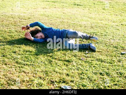 ragazzo di sei anni, scivola giù per una collina erbosa Foto Stock