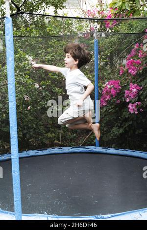 Giovane ragazzo di sei salti su un trampolino Outdoors Model rilascia Foto Stock