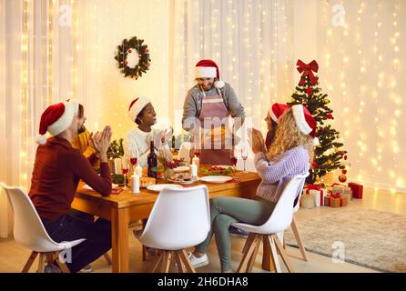 Famiglia e amici che cenano a casa per festeggiare la vigilia di Natale con cibo e decorazioni tradizionali. Foto Stock