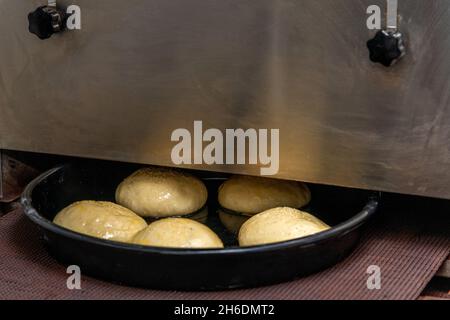 Linea di produzione della cottura. Hamburger crudi non cotti che vanno al forno con il trasportatore. Foto Stock