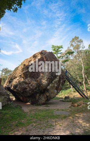 Vista in estate di una donna che sale la scala fissata al Bowder Stone, una roccia di 1.870 tonnellate situata a Borrowdale nel Lake District, Inghilterra, Regno Unito Foto Stock