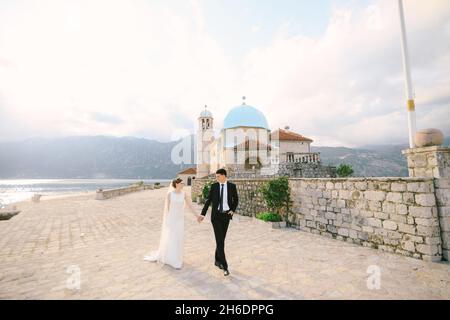 Gli sposi camminano a mano lungo il recinto in pietra della Chiesa della Vergine sull'isola di Gospa od Skrpela Foto Stock