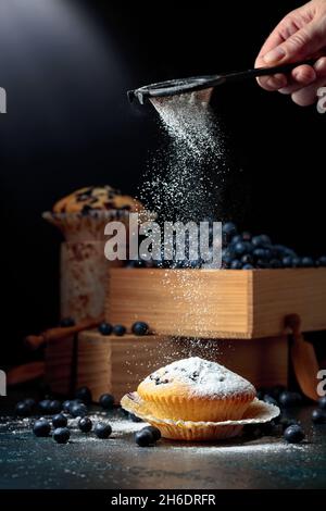Muffin ai mirtilli e frutti di bosco in una scatola di legno. Muffin cosparsi di zucchero in polvere. Foto Stock