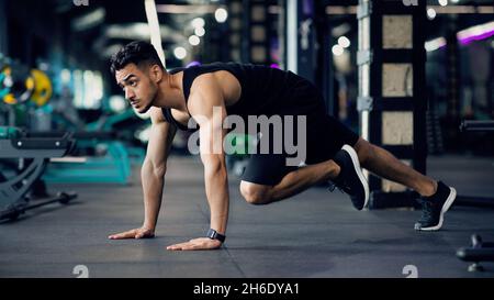 Guy arabo muscolare fiducioso fare esercizio di running Plank durante l'allenamento in palestra Foto Stock