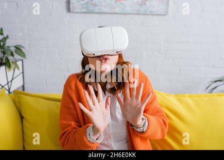 donna spaventata in visore vr che mostra stop gesture durante il gioco a casa Foto Stock