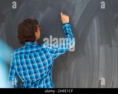 Smart Arab Teen Boy con gesso in mano scrittura su nero bordo vuoto a scuola Foto Stock