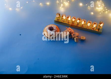 Vacanza ebraica Hanukkah sfondo con menorah tradizionale candelabra, filatura top e ciambella su sfondo blu Foto Stock