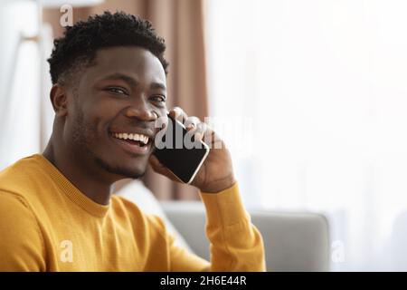 Felice uomo afroamericano seduto sul divano, parlando al telefono Foto Stock