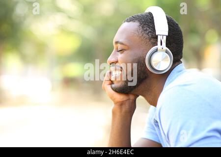 Ritratto del profilo di un uomo felice con pelle nera che ascolta musica con le cuffie in un parco Foto Stock