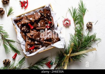 Biscotti al cioccolato in una scatola, rami di pino e giocattoli di Natale su sfondo bianco. Foto Stock