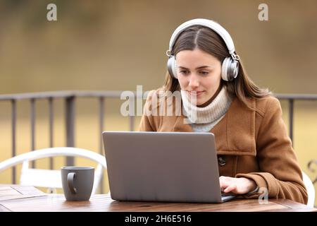 Donna che indossa le cuffie per guardare contenuti multimediali sul laptop in terrazza in inverno Foto Stock