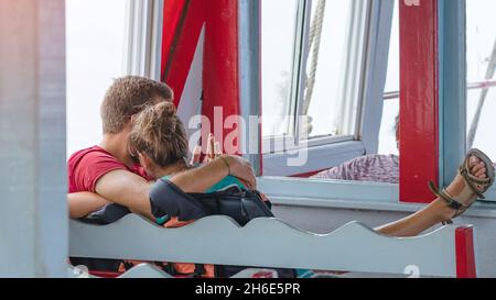 Vista posteriore dei passeggeri amanti della felicità che si abbraccia mentre si rilassano sul balcone godendo la vista dalla barca in mare. Felice coppia di turisti casual su t Foto Stock