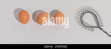 Tre uova e filo di acciaio inossidabile si sussurrano su sfondo bianco Foto Stock