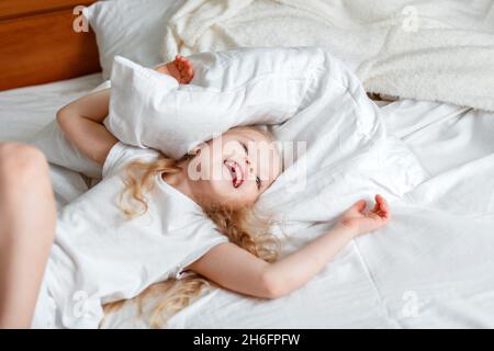 Cheery ragazza piccola di Kid che si diverte saltando nel soggiorno giocando con il cuscino. Ritratto di figlia preschool caucasica bionda ragazza in pigiama giocare Foto Stock