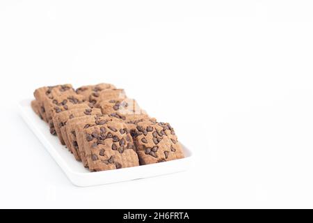 Biscotti a forma quadrata con gocce di cioccolato serviti in vassoio bianco. Isolato su sfondo bianco con spazio di copia per testo personalizzato. Vista frontale chiusura e selezione Foto Stock