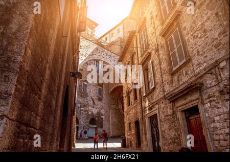 Perugia, Umbria, Italia. Agosto 2020. In un vicolo del centro storico, un arco collega due alti edifici medievali. Persone. Foto Stock