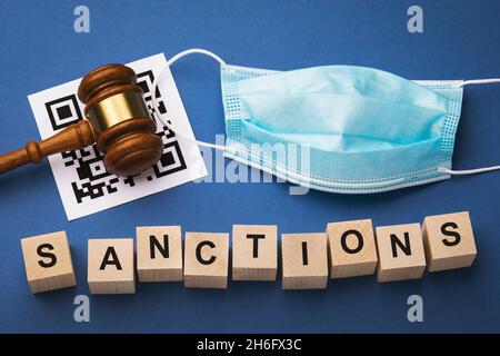 Giudice Gavel, foglio di codice a barre, maschera medica e cubi di legno con testo su sfondo blu, il concetto di sanzioni per violazione dei codici QR regim Foto Stock
