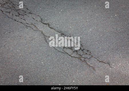 I veicoli passano un buco della pentola e la superficie della strada danneggiata a Godley Cutting, Halifax, West Yorkshire, Regno Unito. Una pothole è una depressione in una superficie stradale, di solito asfalto pavimentazione, dove il traffico ha rimosso pezzi rotti del marciapiede. È solitamente il risultato di acqua nella struttura di suolo sottostante e traffico che passa sopra l'area colpita. L'acqua prima indebolisce il terreno sottostante; il traffico poi si affatica e rompe la superficie di asfalto mal sostenuta nell'area colpita. L'azione continua del traffico espelle sia l'asfalto che il materiale del terreno sottostante per creare un buco nel marciapiede. Foto Stock