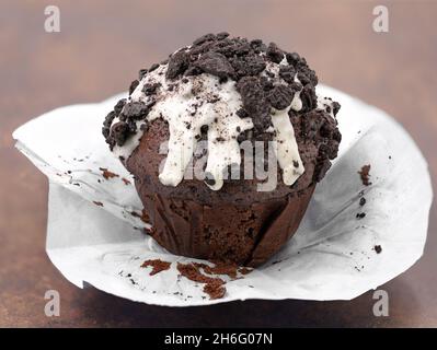 muffin al cioccolato con glassa bianca e biscotti scuri grattugiati su sfondo marrone, cupcake non imballato Foto Stock