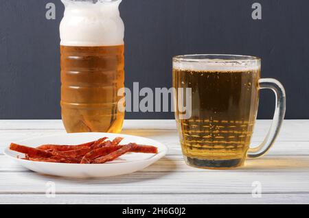 Ancora vita con la birra versata in una tazza e fette di pesce essiccato su una piastra di porcellana Foto Stock