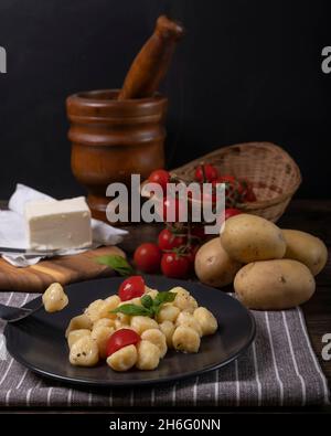 Un piatto di gnocchi di patate con pomodori ciliegini rossi con un mortaio di legno sullo sfondo Foto Stock