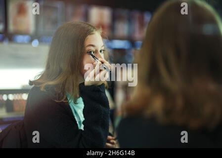 Ragazza adolescente che prova i prodotti cosmetici nel negozio di cosmetici. Fare il make-up. Foto Stock