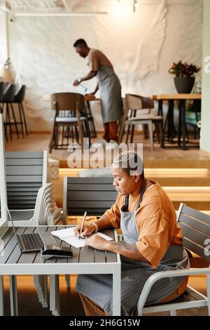 Vista laterale di giovane uomo e donna che lavorano in un moderno caffè preparare mobili e prendere appunti prima di aprire Foto Stock