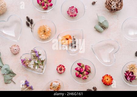 Ornamenti fai-da-te riempiti di fiori secchi su fondo di cemento beige. Albero di Natale o idea di decorazione di San Valentino. Vista dall'alto, piatto Foto Stock