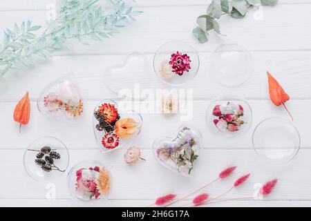 Ornamenti fai-da-te riempiti di fiori secchi su sfondo bianco in legno. Albero di Natale decorazione idea. Vista dall'alto, piatto. Foto Stock