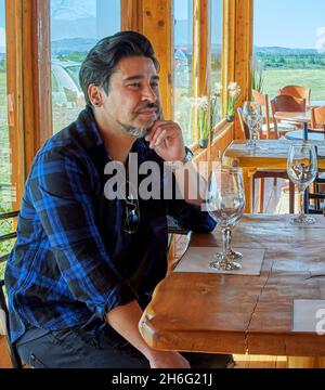 Bruna ragazzo latino in attesa di un bicchiere o vino in una prova di vino. Visita guidata di un vigneto durante la vacanza a Cordoba Argentina. Verticale Foto Stock