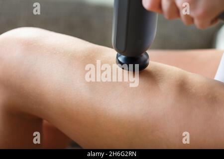 Auto-massaggio delle gambe delle donne con una pistola perfezionante a casa. Massaggio antiurto per ripristinare i muscoli della plancia e i punti di attivazione Foto Stock