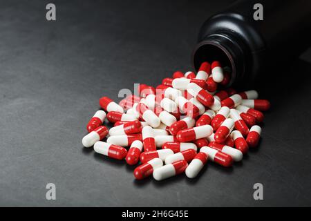 Pillole con farmaci sono sparsi da un vaso nero su uno sfondo nero. Si tratta di una forma di dosaggio solida dosata per somministrazione orale Foto Stock