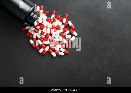 Pillole con farmaci sono sparsi da un vaso nero su uno sfondo nero. Si tratta di una forma di dosaggio solida dosata per somministrazione orale Foto Stock