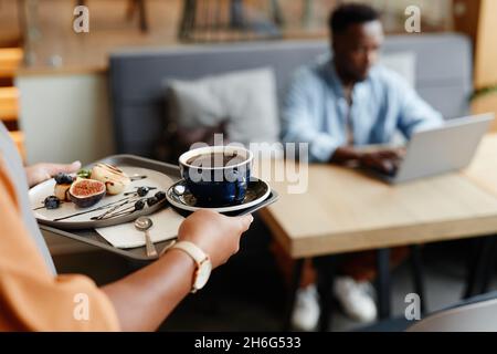 Focus shot selettivo di donna irriconoscibile che lavora in caffè portando caffè e dessert ai giovani clienti Foto Stock