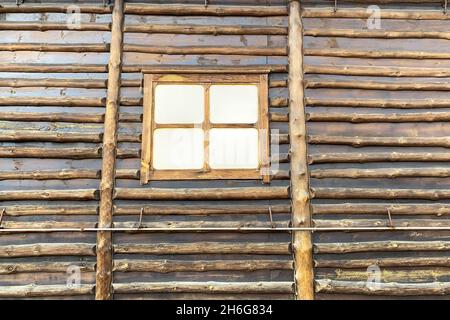 Semplice casa di campagna in legno e tronchi con finestra chiusa. Abitazione abbandonata vuota. Primo piano. All'aperto. Foto Stock