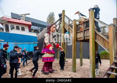 Little Amal è visto avvicinarsi ad un uccello burattino posto in un parco giochi.Amare, un nuovo centro culturale nel centro dell'Aia ha organizzato come parte del suo 'Open Festival', la visita del gigante burattino 'Little Amal', Una bambina di rifugiati siriani di nove anni e alta oltre 11 metri fino al parco in miniatura, Madurodam. È invitata a partecipare al Festival come ospite speciale della città per attirare l'attenzione in tutta Europa sulla situazione dei giovani rifugiati fuggiti dalla Siria. Amal è stata ricevuta fuori dal parco da un gruppo di bambini, dopo di che poteva camminare intorno alle repliche modello in scala 1:25 Foto Stock