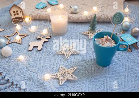 Bello sfondo di natale accogliente con ghirlande, una candela in un bicchiere, una tazza su una maglia blu plaid Foto Stock