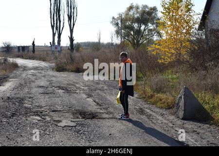 Un adolescente si trova sulla strada alla periferia di Verkhnotoretske Village.Verkhnotoretske è un insediamento ucraino di tipo urbano situato sulla prima linea nel distretto di Yasynuvata, nell'oblast di Donetsk dell'Ucraina orientale. Durante la guerra di Donbas, iniziata a metà aprile 2014, la linea di separazione tra le parti in guerra è stata situata nelle vicinanze dell'insediamento. Il villaggio era una zona grigia fino alla fine del 2017. Oggi Verkhnotoretske è un territorio ucraino. Il conflitto ha provocato vittime civili e militari. Foto Stock