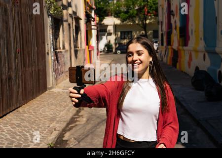 Bella Latina Influencer con occhi grigi che registra un video post con il suo cellulare per caricare sui social network. Concetto di comunicazione visiva, Foto Stock