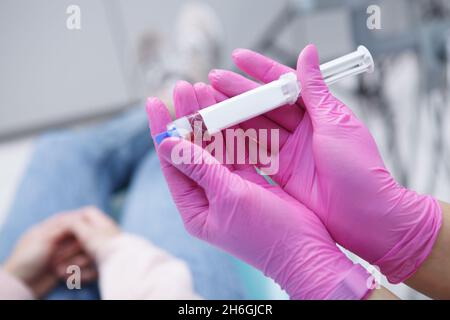 Primo piano corto dei denti tubo di gel sbiancante nelle mani di dentista irriconoscibile che indossa guanti di gomma rosa Foto Stock