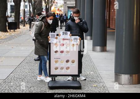 Berlino, Germania. 15 Nov 2021. La gente guarda un menu con un avviso delle attuali misure COVID-19 all'esterno di un negozio di ciambelle a Berlino, in Germania, il 15 novembre 2021. A causa del rapido aumento dei nuovi casi COVID-19, lunedì Berlino ha iniziato a rafforzare le misure COVID-19. Il tasso di incidenza di sette giorni della Germania ha raggiunto un nuovo picco storico e ha raggiunto 303.0 per 100,000 abitanti, il Robert Koch Institute (RKI) per le malattie infettive annunciato lunedì. Credit: Shan Yuqi/Xinhua/Alamy Live News Foto Stock