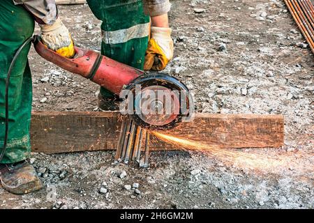 Una mano maschio taglia pezzi di rinforzo con una smerigliatrice angolare. Taglio dell'acciaio inframezzato da scintille in cantiere. Scintille quando si tagliano Foto Stock