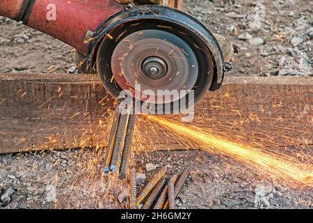 Una mano maschio taglia pezzi di rinforzo con una smerigliatrice angolare. Taglio dell'acciaio inframezzato da scintille in cantiere. Scintille quando si tagliano Foto Stock