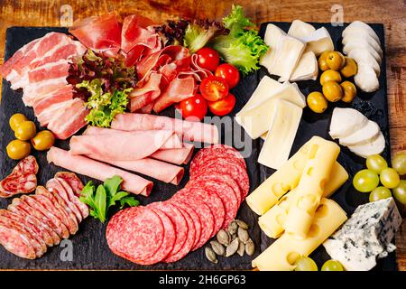Salumi, antipasti con assortimento di salumi, formaggi, camembert e olive su tavola di legno. Vari tipi di carne e salsicce su legno Foto Stock