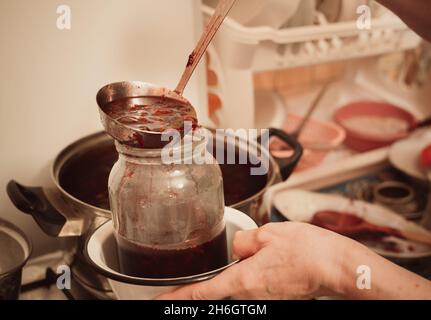 Mettendo la marmellata calda in un vaso di vetro da una pentola grande sul fornello Foto Stock