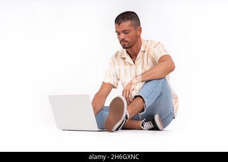 Giovane uomo seduto a terra con il suo computer portatile Foto Stock
