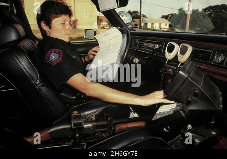 Austin Texas USA, circa 1994: Funzionario di polizia ispanica femminile che lavora sul suo computer nella sua macchina di pattuglia. ©Bob Daemmrich Foto Stock