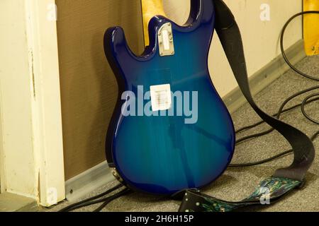 Una chitarra elettrica blu si trova contro un muro in uno studio musicale professionale. Il lato opposto della chitarra. Strumento musicale a corde firmato Foto Stock