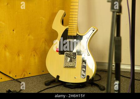 Una chitarra elettrica gialla si trova contro un muro in uno studio musicale professionale. Strumento musicale firmato a corde di colore brillante. Acustica perfetta Foto Stock